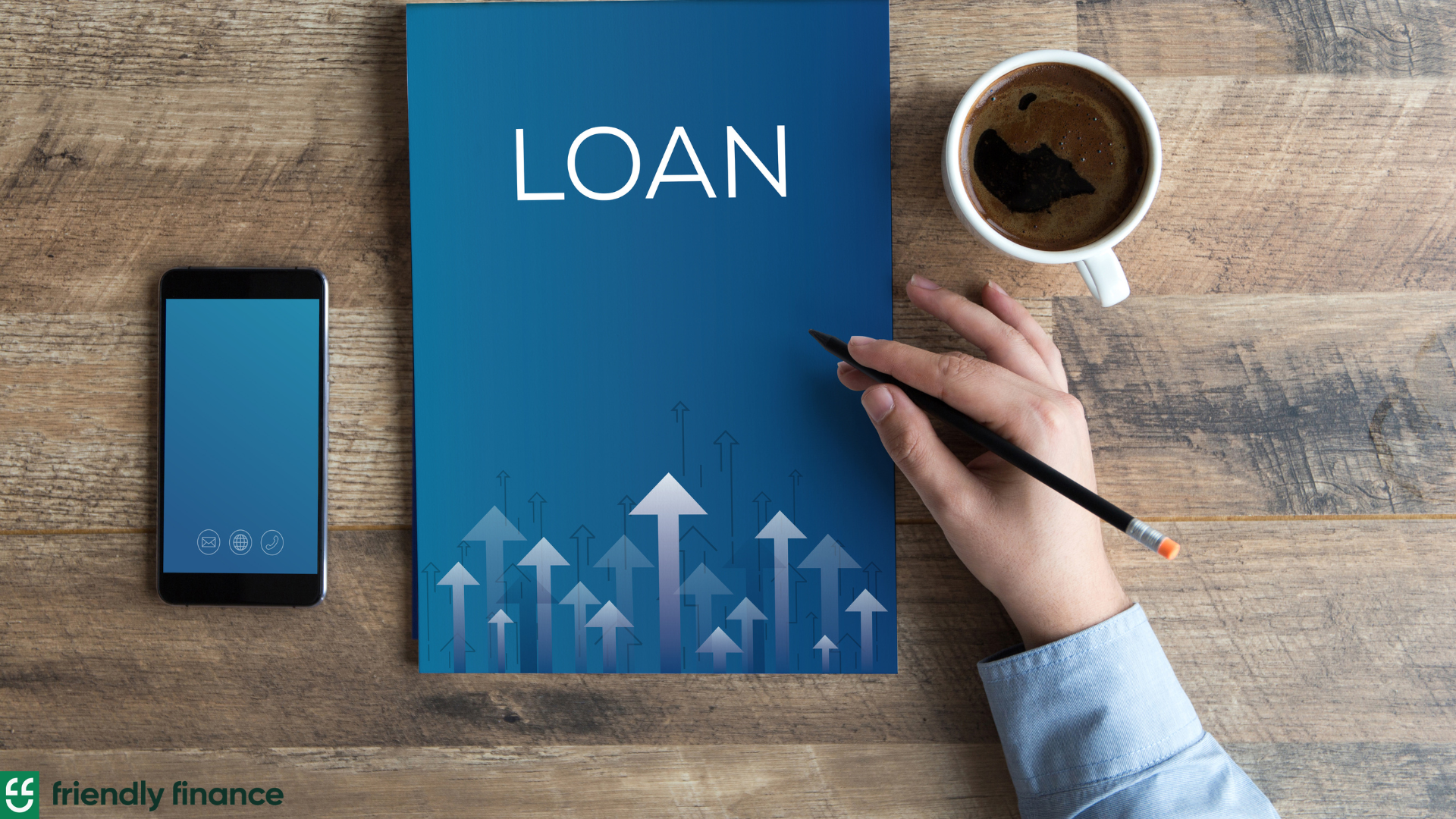 A booklet with "Loan" as title; beside the book on the left is a mobile phone and on the right is a coffee mug. A visible hand of a man holding a pen is placed near the loan booklet