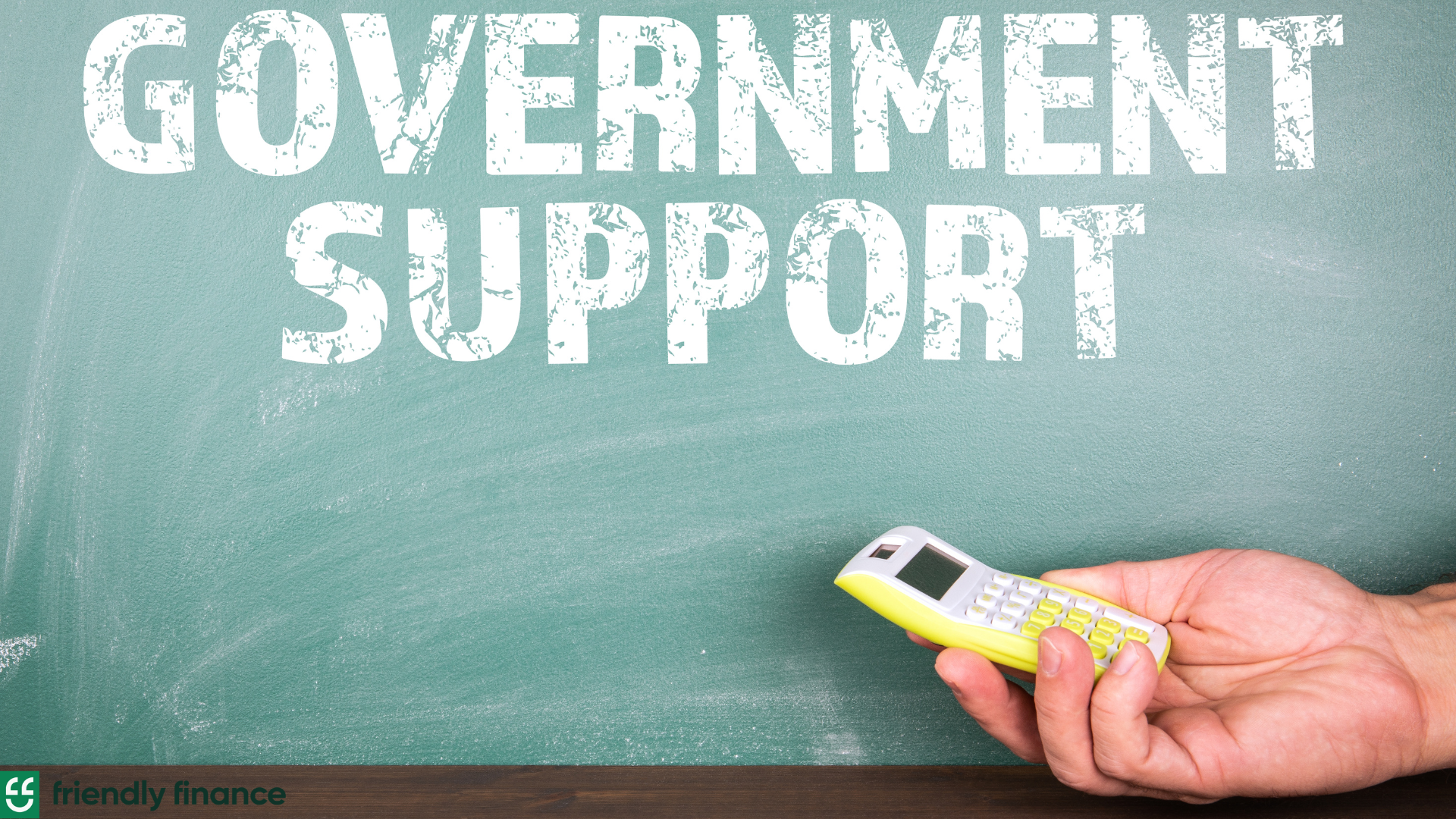 a chalk board with the words "Government Support" written; a visible hand holding a calculator is rested below